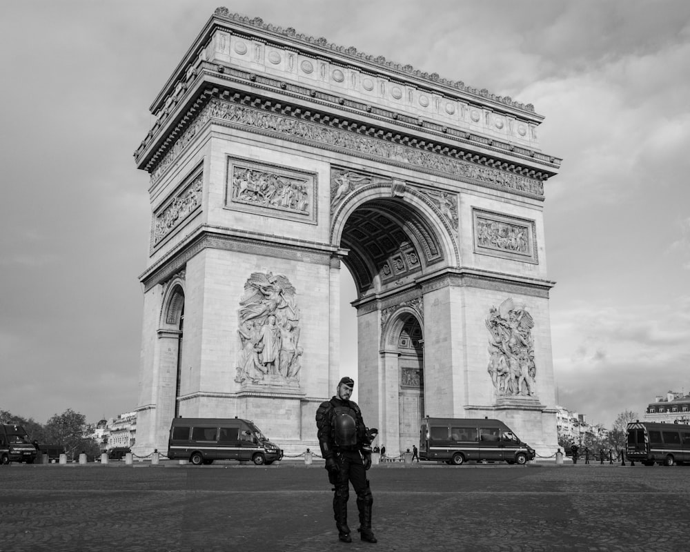 photographie en niveaux de gris d’un homme debout près de l’Arc de Triomphe