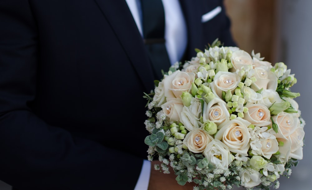 man wearing black suit holding white rose bouquet