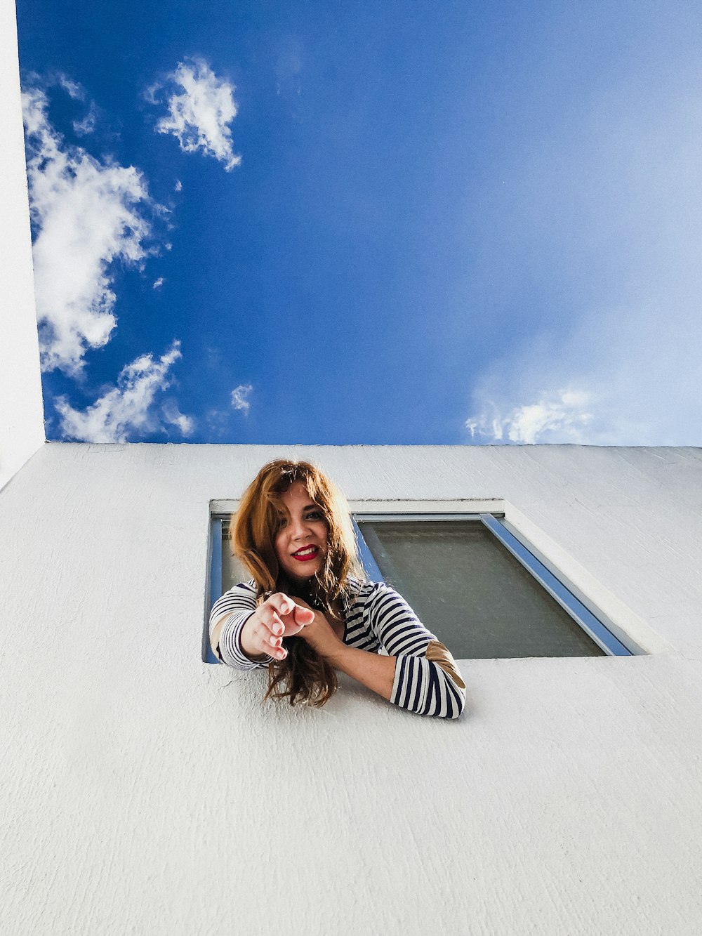 woman on window reaching her hands down under blue sky