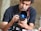 A person is closely examining a Canon DSLR camera with attention. The camera lens reflects what appears to be a distant scene or light source, giving it a captivating glow.