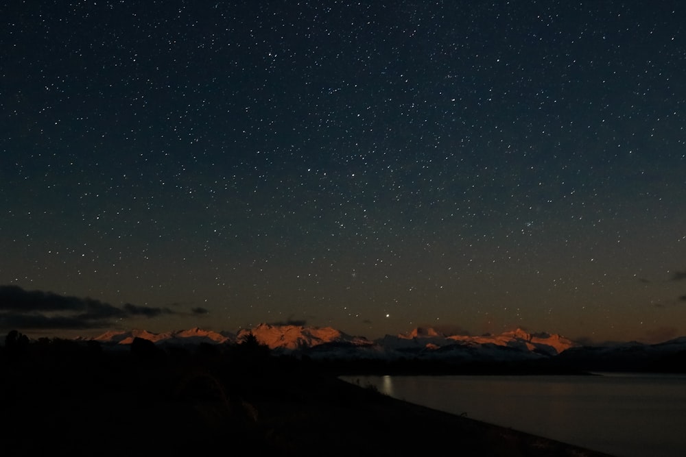 Fotografía de paisaje de cielo despejado lleno de estrellas sobre montañas durante la noche