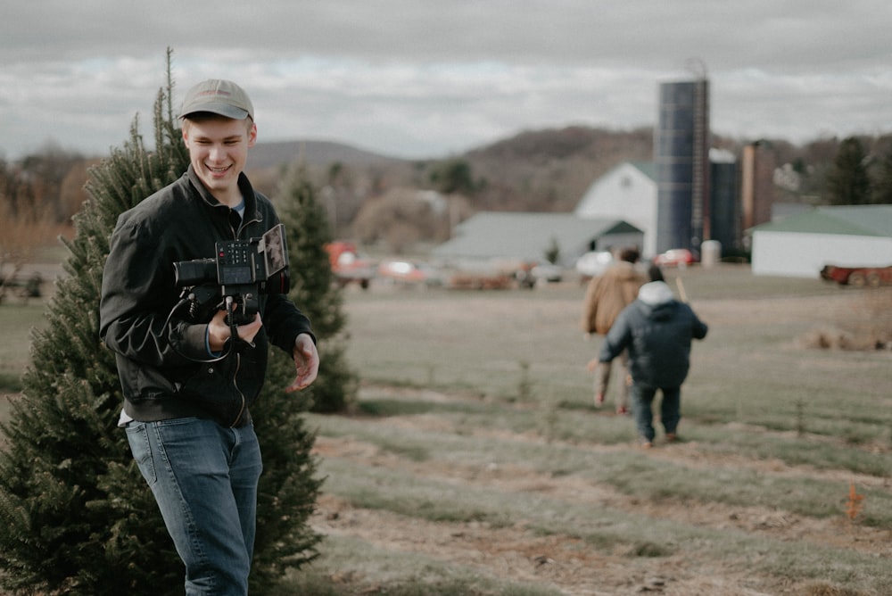 man holding video camera standing near green bush