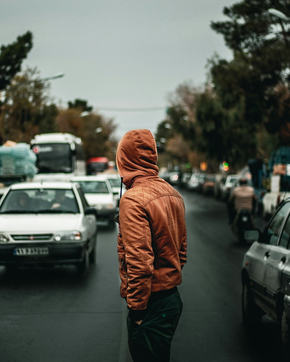 man standing in center of road beside passing vehicles at daytime