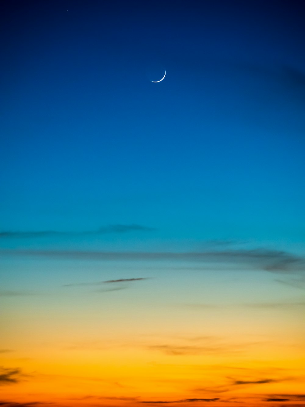 Mondsichel und blauer Himmel während der Goldenen Stunde