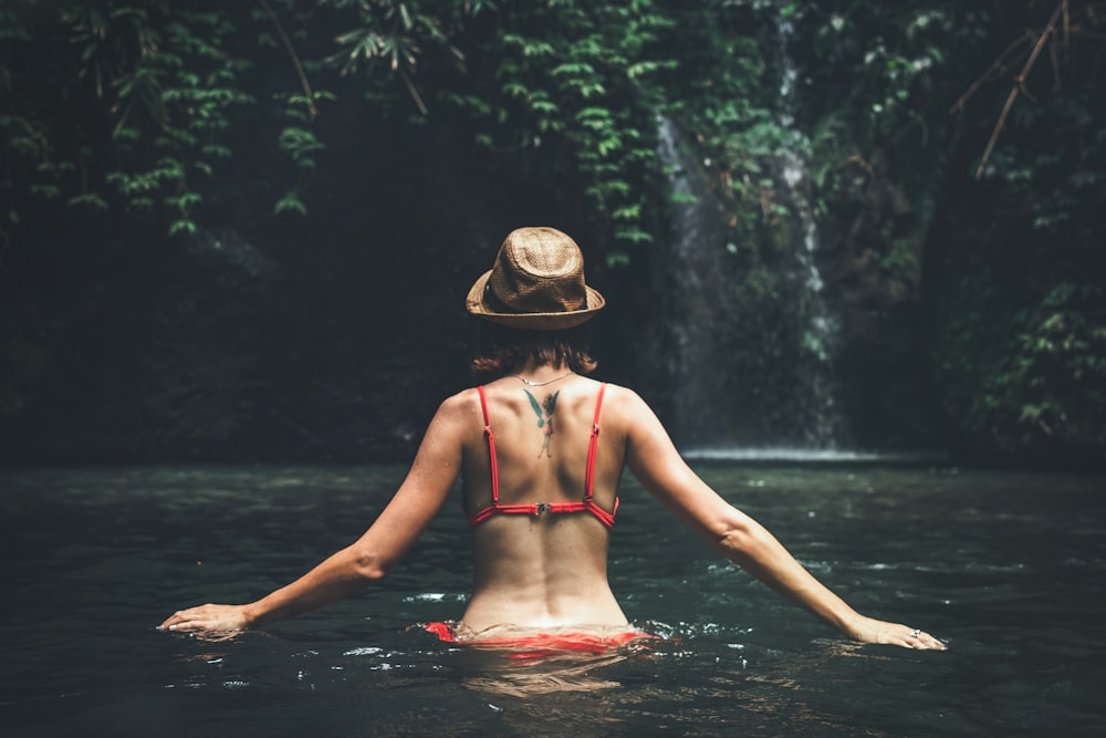 woman in red 2-piece walking near waterfalls during daytime