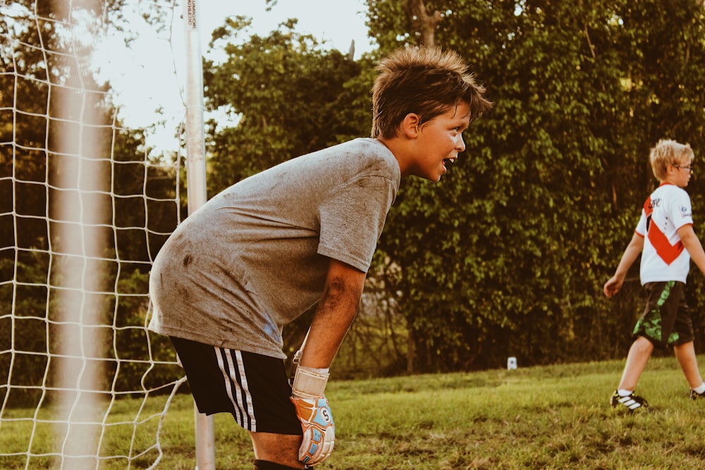 boy wearing grey shirt standing near goalie net