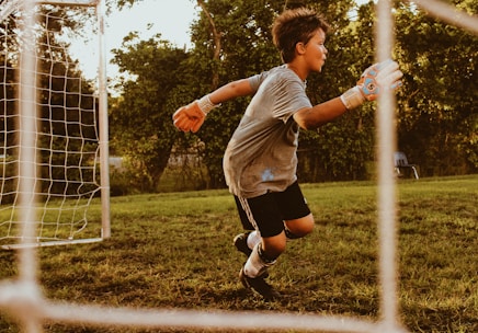 Young Brazilian athlete training on a soccer field with an American university stadium in the background.