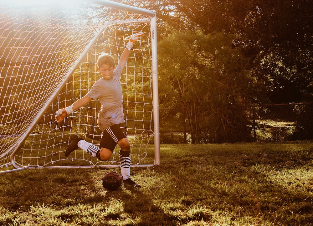 menino chutando bola de futebol preta ao lado do gol de futebol