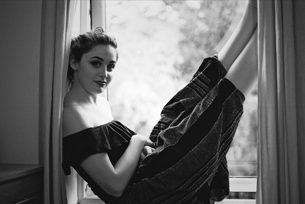 grayscale photography of woman sitting on window