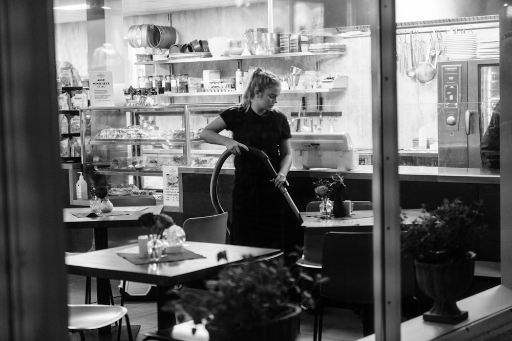 grayscale photography of woman vacuuming under table