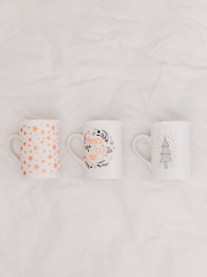 three white-and-multicolored ceramic mugs on white textile