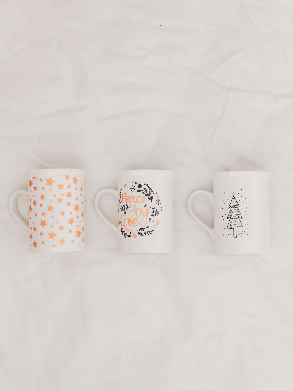 three white-and-multicolored ceramic mugs on white textile