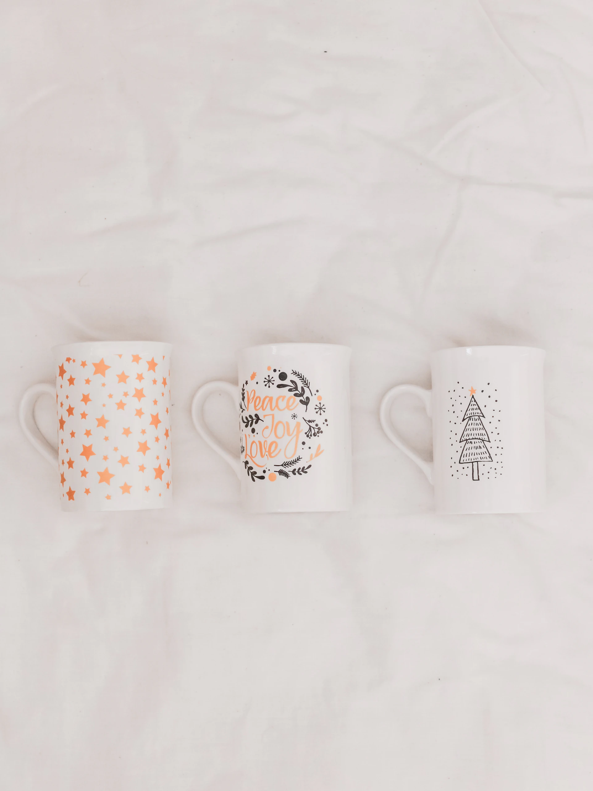 three white-and-multicolored ceramic mugs on white textile