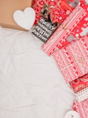 A collection of festive packaging, including boxes and wrapped gifts. The wrapping paper features red and white designs with Christmas motifs such as snowflakes and reindeer. There's also a small black bag with the words 'Merry and Bright Festive Funstuff'. A cardboard box and a heart-shaped object with the word 'Faith' are visible.