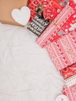 A collection of festive packaging, including boxes and wrapped gifts. The wrapping paper features red and white designs with Christmas motifs such as snowflakes and reindeer. There's also a small black bag with the words 'Merry and Bright Festive Funstuff'. A cardboard box and a heart-shaped object with the word 'Faith' are visible.