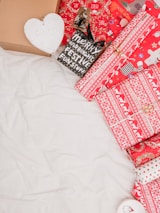 A collection of festive packaging, including boxes and wrapped gifts. The wrapping paper features red and white designs with Christmas motifs such as snowflakes and reindeer. There's also a small black bag with the words 'Merry and Bright Festive Funstuff'. A cardboard box and a heart-shaped object with the word 'Faith' are visible.