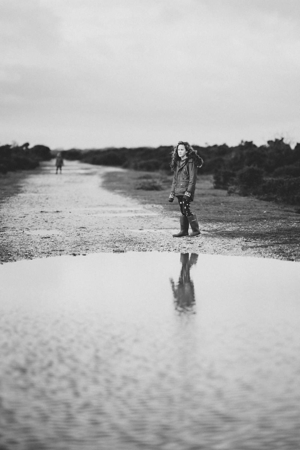 grayscale photography of girl standing near water puddle