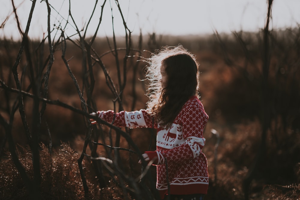 selective focus of girl standing beside leafless trees near grasses