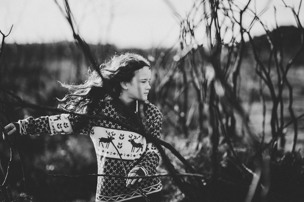 grayscale photo of girl near bare trees