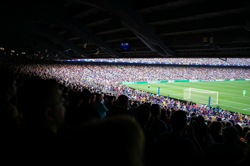 A vibrant crowd wearing colorful team jerseys cheering wildly at a packed stadium during a soccer match.