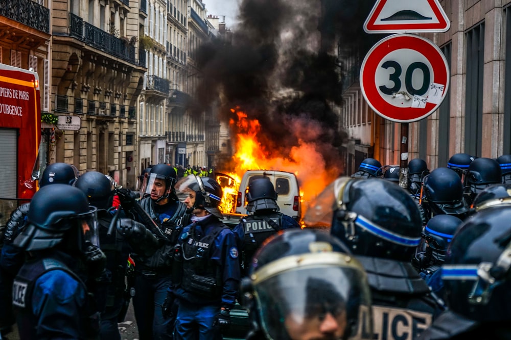 black smoke emitting from fire on road in front of Police wearing headgear during daytime