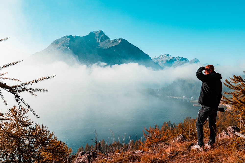 homem de pé perto da borda de uma montanha de frente para as montanhas durante o dia