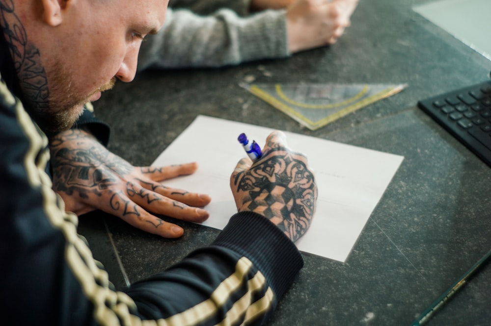 man with tattoos holding blue pen