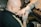 A person with tattooed hands is working on another person's hand, which is wrapped for protection. The setting has a focused and artistic atmosphere, likely in a tattoo studio.
