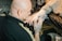 A person with tattooed hands is working on another person's hand, which is wrapped for protection. The setting has a focused and artistic atmosphere, likely in a tattoo studio.