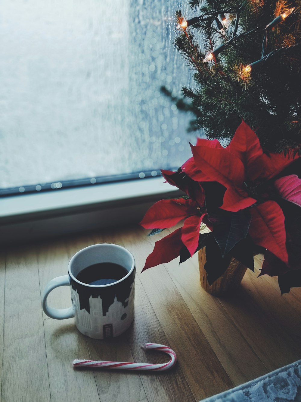 窓際のクリスマスツリーのそばにあるマグカップのコ��ーヒー