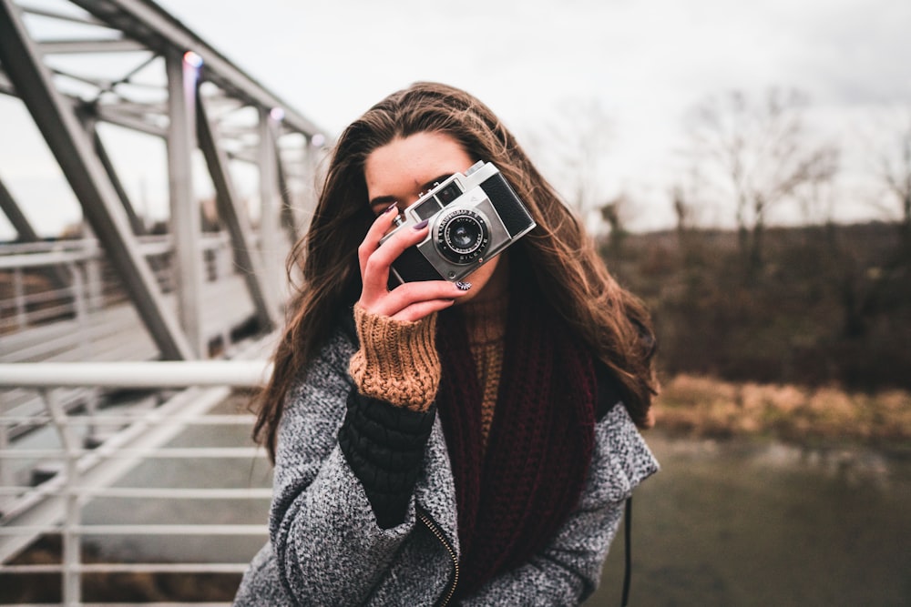 woman using camera leaning on handrail near bridge