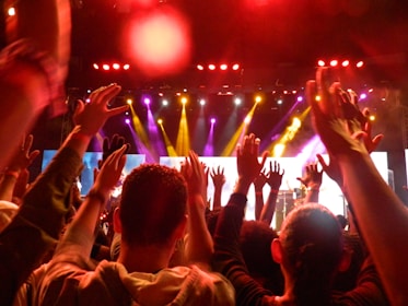 An intense close-up of a live concert crowd, hands raised and faces lit by stage lights.