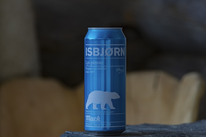 A blue can with white text and a graphic of a polar bear is prominently displayed. The can rests on a textured stone surface, with a blurred background that appears to be wooden or earthy.