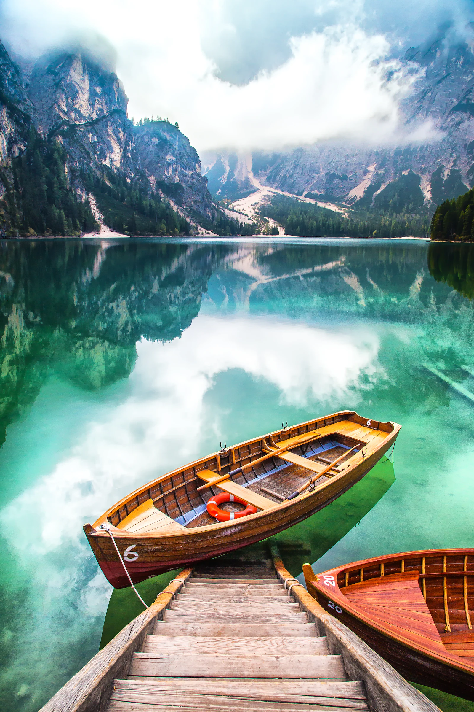 Wooden rowing boats moored on a still alpine lake below mist-covered peaks