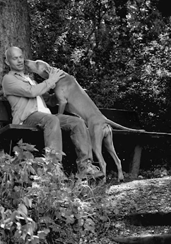 Andre smiling warmly while sitting on a park bench with a relaxed dog beside him.
