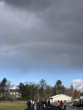 A vibrant softball game under a rainbow sky with players celebrating a great play.