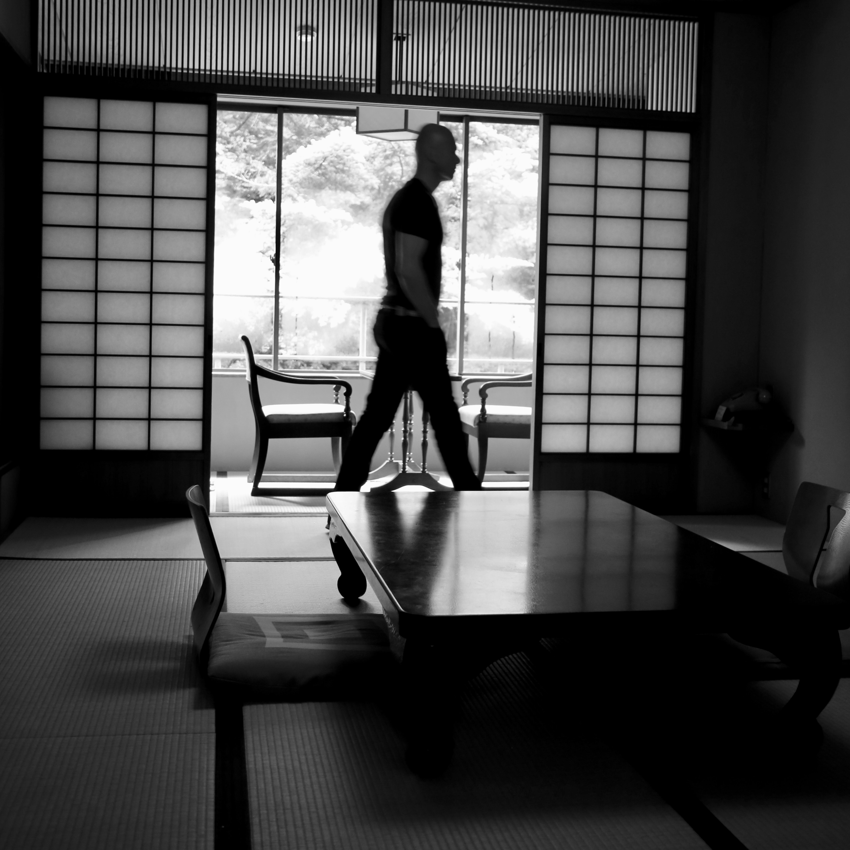 grayscale photo of man walking near shoji screens