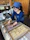 Photo of a woman in a traditional apron arranging sweets in her shop with milk bottles on the counter.