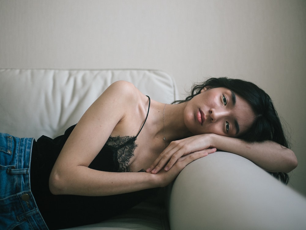 woman wearing black spaghetti-strap tank top and blue denim bottoms lying on sofa