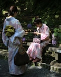two women wearing floral dress standing and sitting near flowers