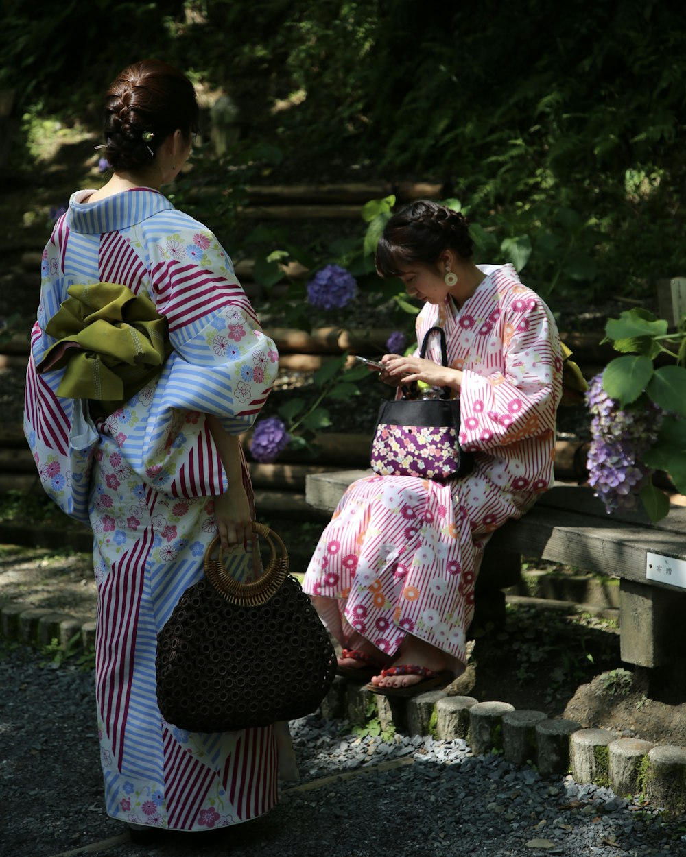 two women wearing floral dress standing and sitting near flowers