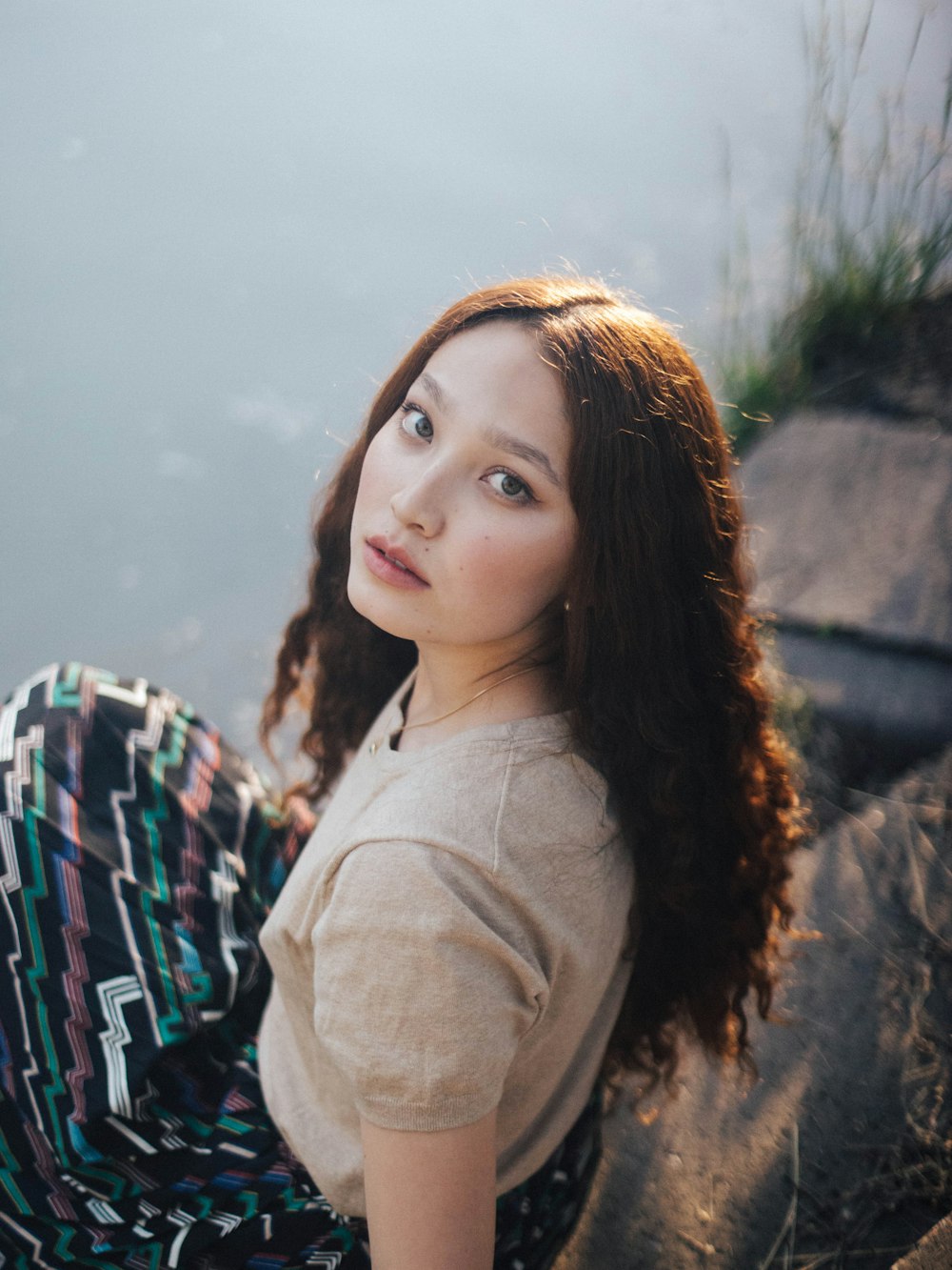 woman in grey shirt sits on river bank