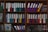 A wooden shelf is filled with various colorful ring binders and folders neatly organized. The binders have labels with text on them and are stacked both horizontally and vertically. Some loose papers and additional documents are tucked among the folders. The scene suggests an office or study environment with a focus on organization.