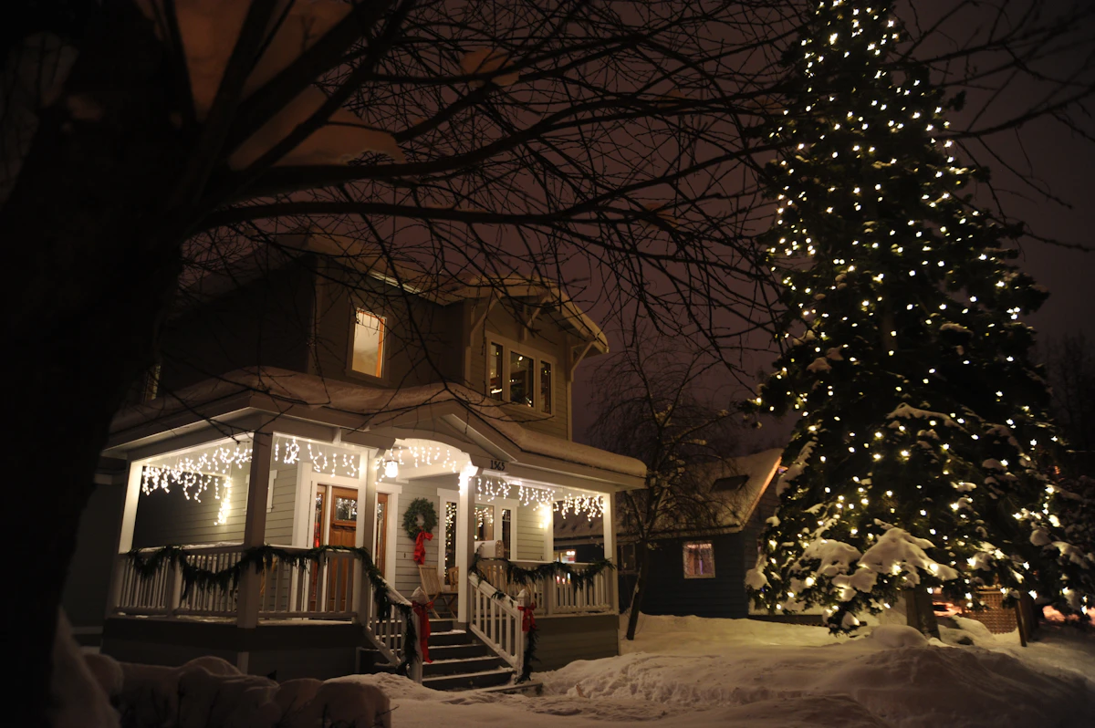 Porch icicle lights and a lit Christmas tree beside a house