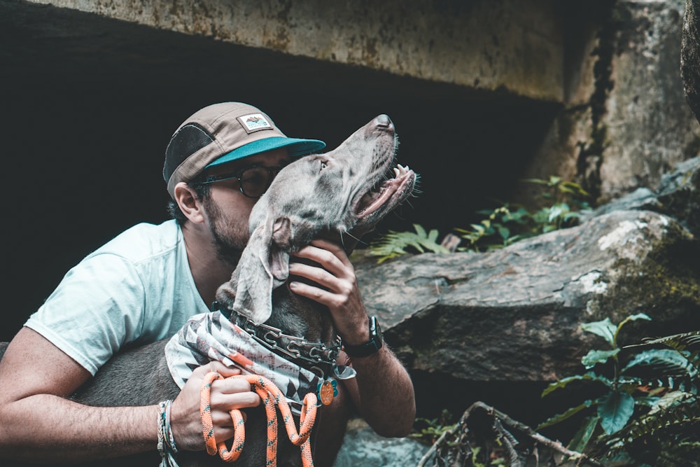 person wearing cap holding short-coated dog during daytime