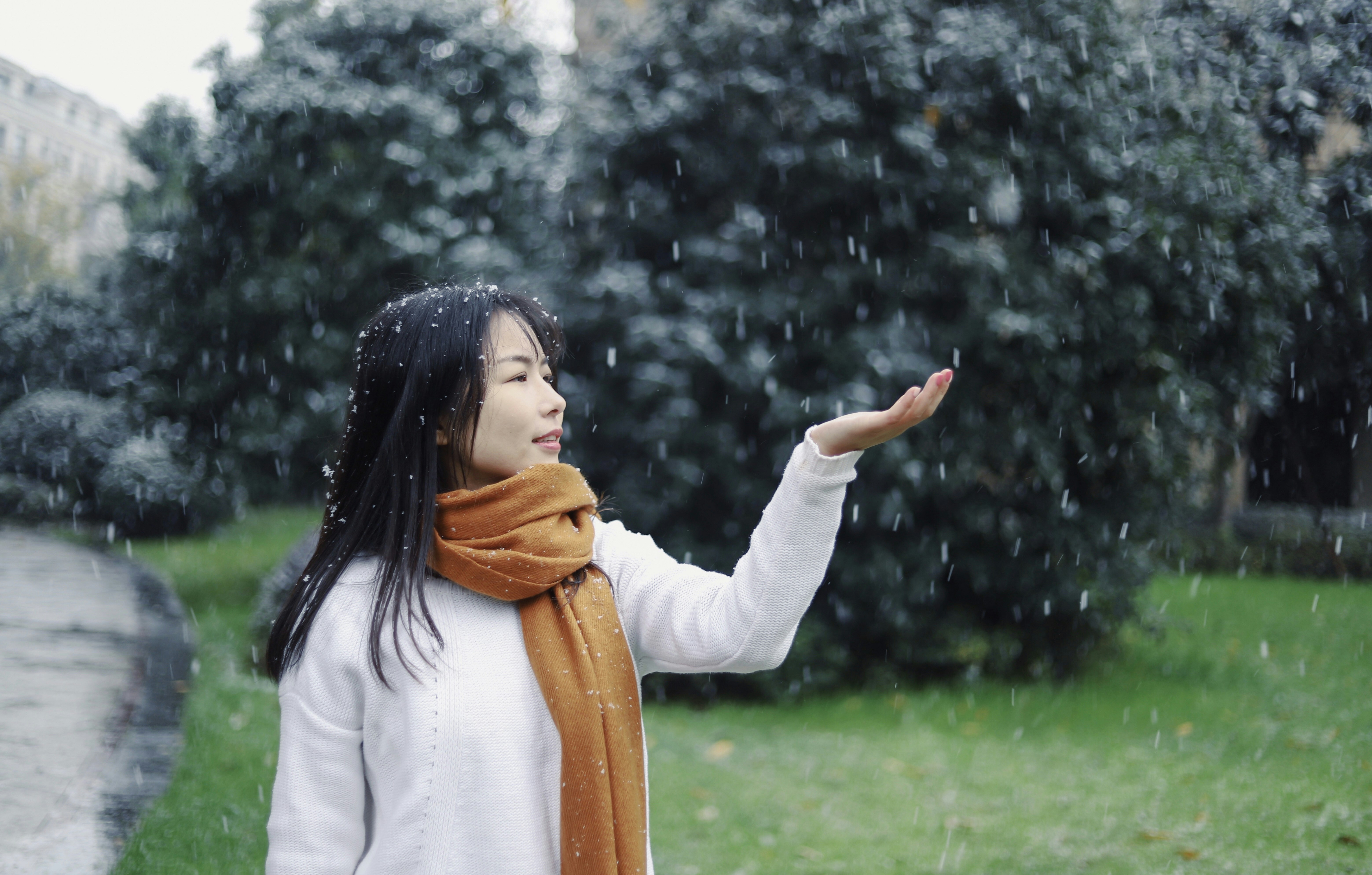 Woman in white long-sleeved sweater and brown scarf catching snow ...