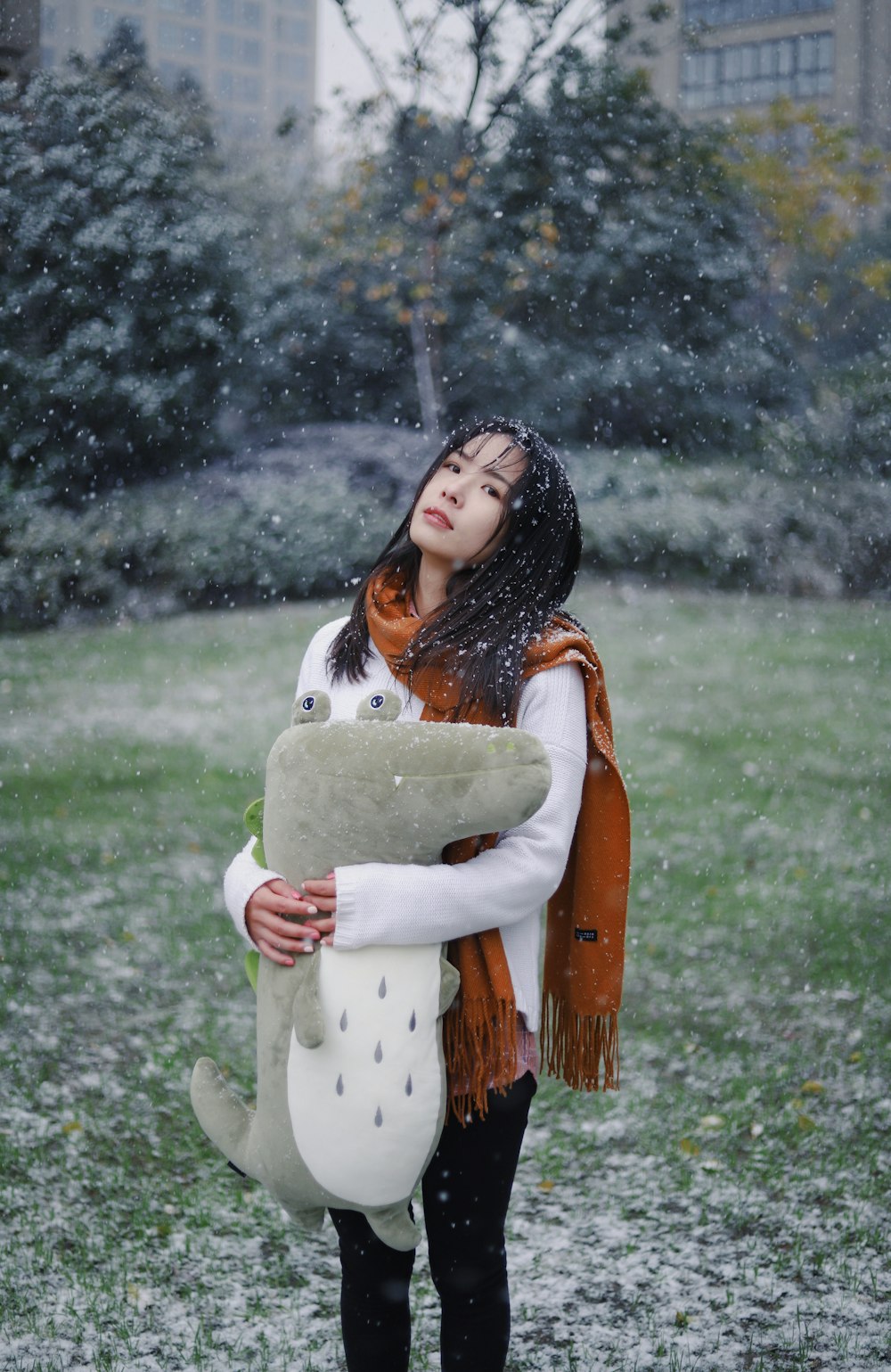 woman wearing white long-sleeved shirt, brown fringe scarf and holding gray plush toy during snowy daytime
