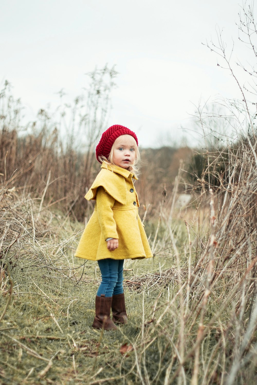 Menina vestindo casaco amarelo em pé no campo de grama