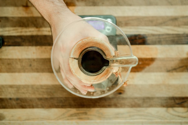 a hand holding a glass container on top of a striped wood table