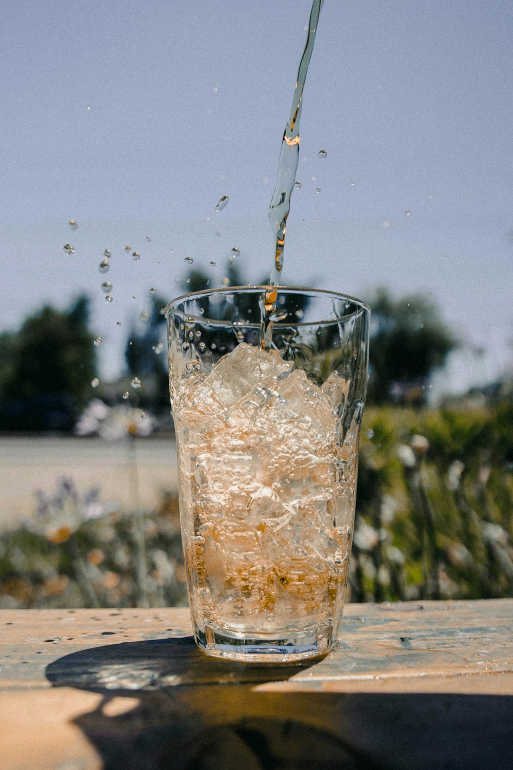 klares Trinkglas mit Eiswürfeln und fließender Flüssigkeit tagsüber